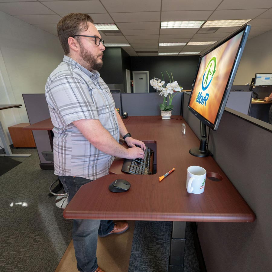 Working at a Lander Standing L-Desk with SteadyType. Clove Mahogany desktop on Black base.